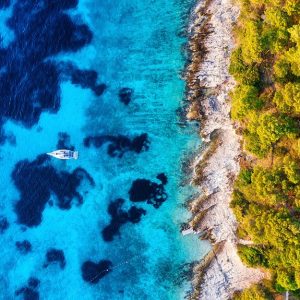 Blue Water Background And Coast With Forest From Top View. Yacht